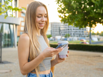 Blonde hair woman smiles at phone screen texting message standing in the street at sunset