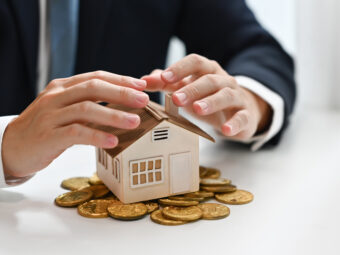 Businessman hands protecting house model and pile of gold coins. Real estate, property investment and save money concept